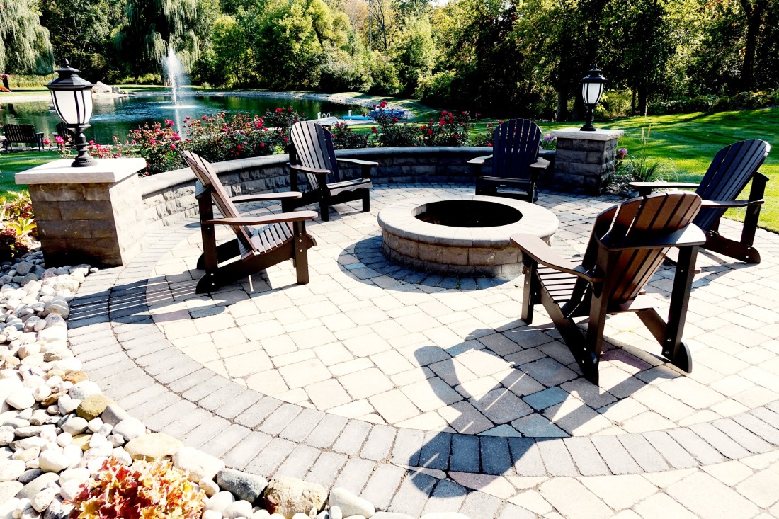 A large lawn with beautiful landscaping feature a pond and cobblestone seating area
